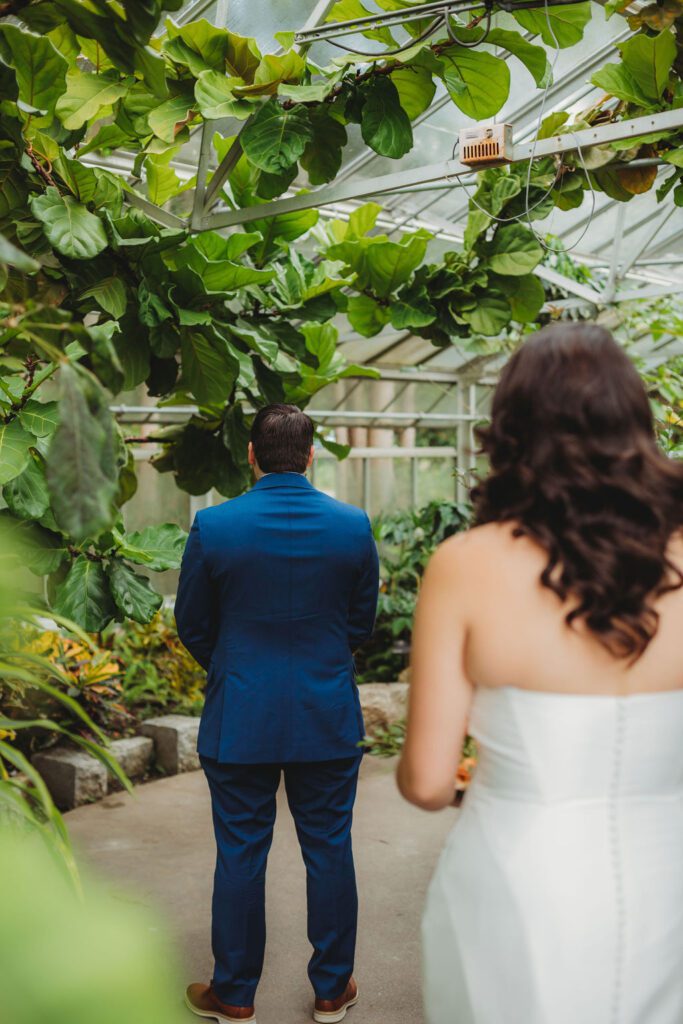 Bride walking towards groom during first look in greenhouse at Roger Williams Botanical Garden Park in Providence, Rhode Island.