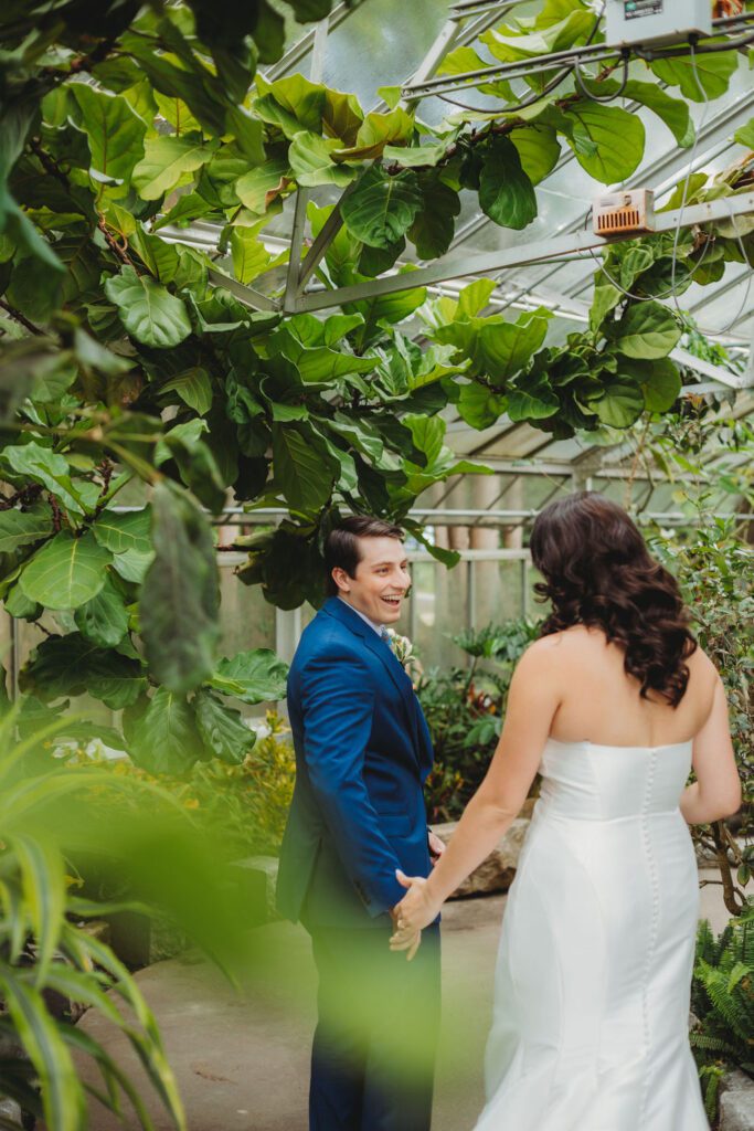 Groom smiling as he sees bride during their romantic first look in a greenhouse at Roger Williams Botanical Garden Park in Providence, Rhode Island.