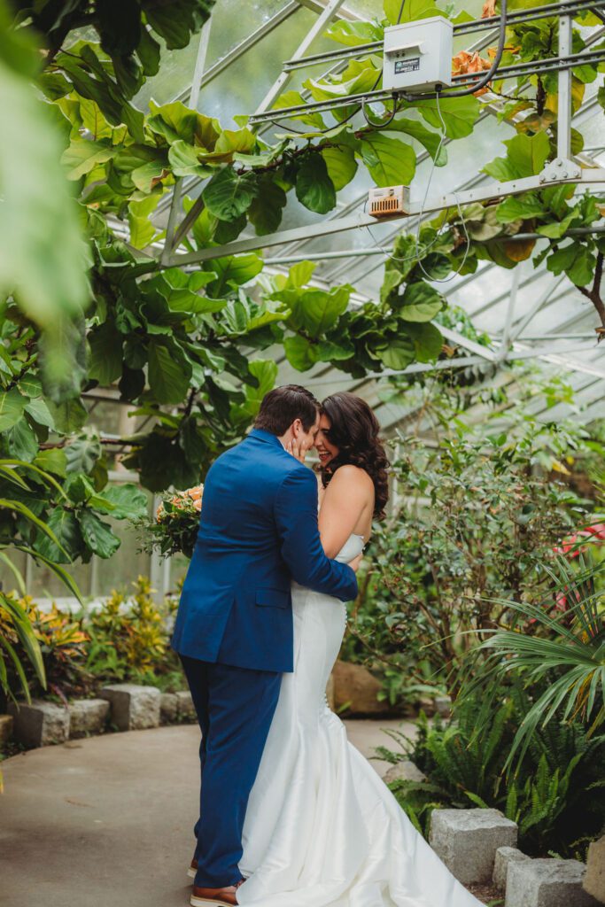 Bride and groom kiss during romantic first look in a greenhouse at Roger Williams Botanical Garden Park in Providence, Rhode Island.