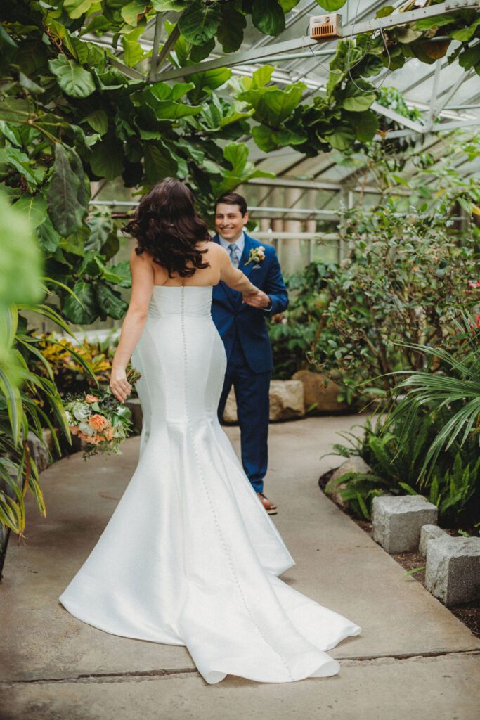 Groom smiling at a bride as he holds her hand an leads her into the greenhouse at Roger Williams Botanical Garden Park in Providence, Rhode Island.