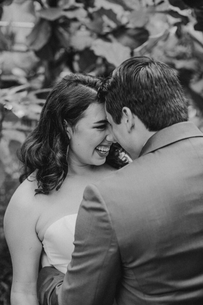 Bride and groom have their foreheads touching as the bride smiles and laughs in a greenhouse at Roger Williams Botanical Garden Park in Providence, Rhode Island.