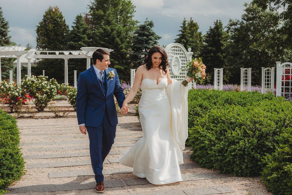 Groom is looking at bride and they are both smiling as they walk through the flower garden at Roger Williams Botanical Garden Park in Providence, Rhode Island.