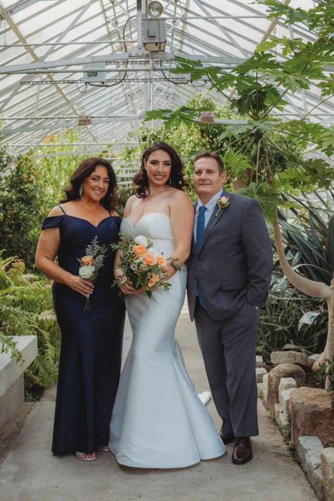 Bride and her parents smiling in a greenhouse for family formals at Roger Williams Botanical Garden Park in Providence, Rhode Island.