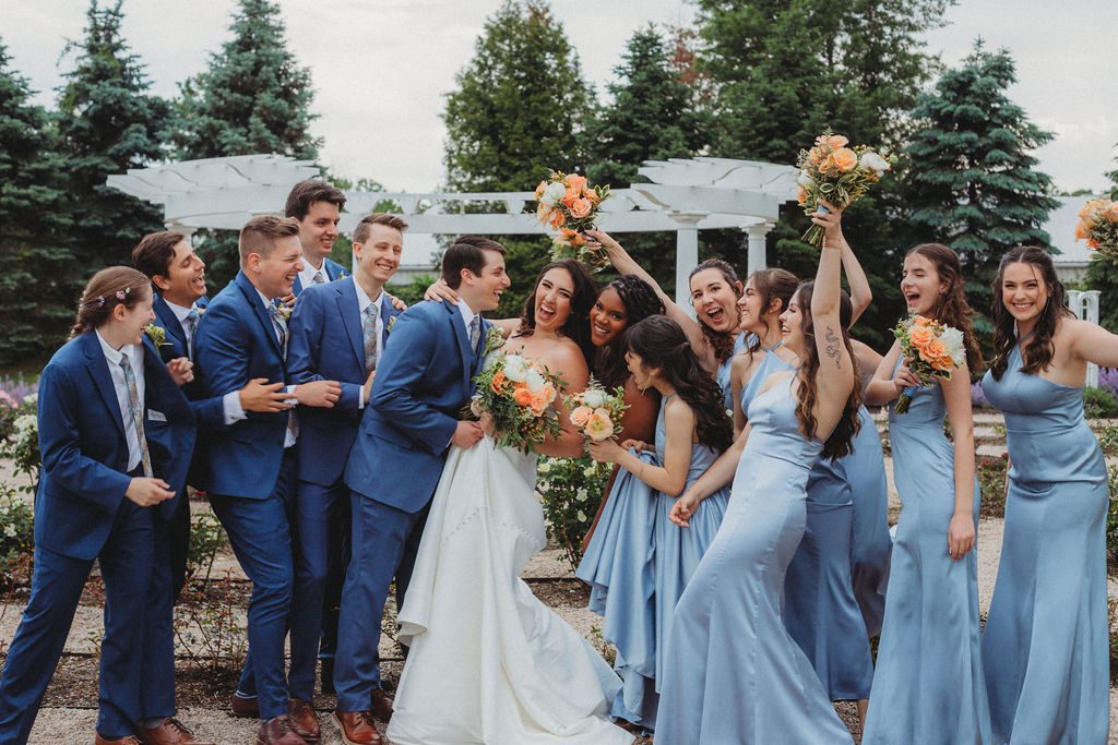 Bridal party running towards the bride and groom while they smile and laugh in rose garden at Roger Williams Botanical Garden Park in Providence, Rhode Island.