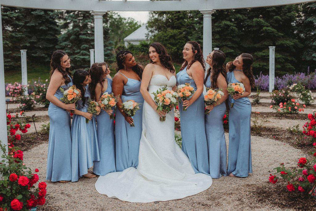 Bride smiling with her bridesmaids in the rose garden at Roger Williams Botanical Garden Park in Providence, Rhode Island.