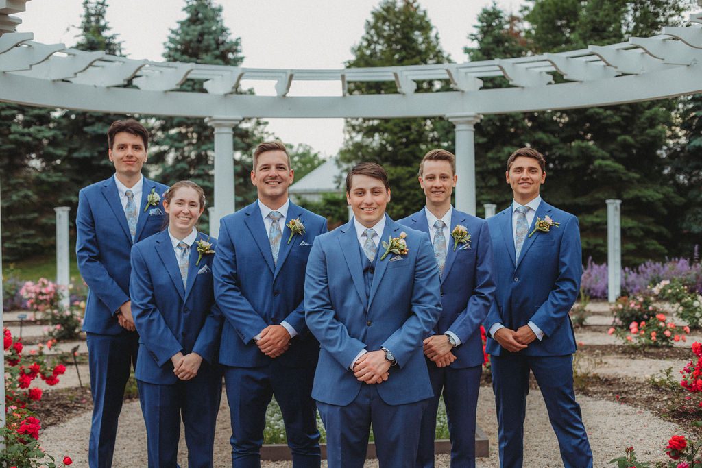 Groom and groomsmen smiling in a line the rose garden at Roger Williams Botanical Garden Park in Providence, Rhode Island.