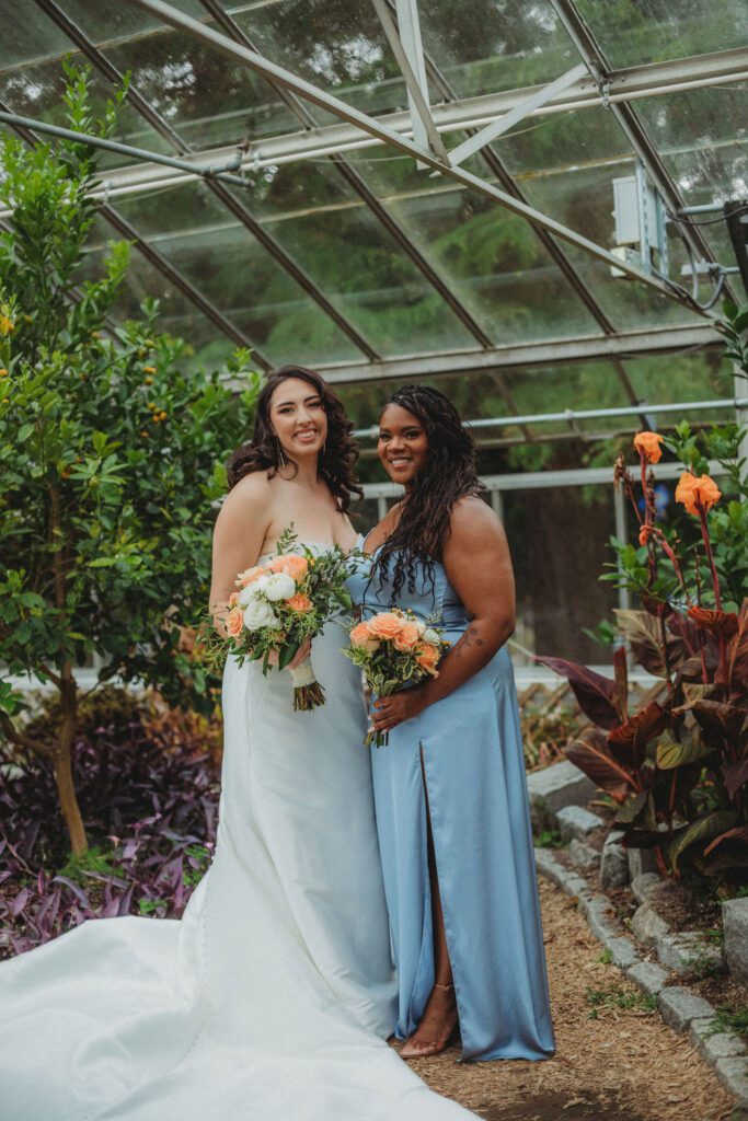 Bride and maid of honor smiling in greenhouse at Roger Williams Botanical Garden Park in Providence, Rhode Island.