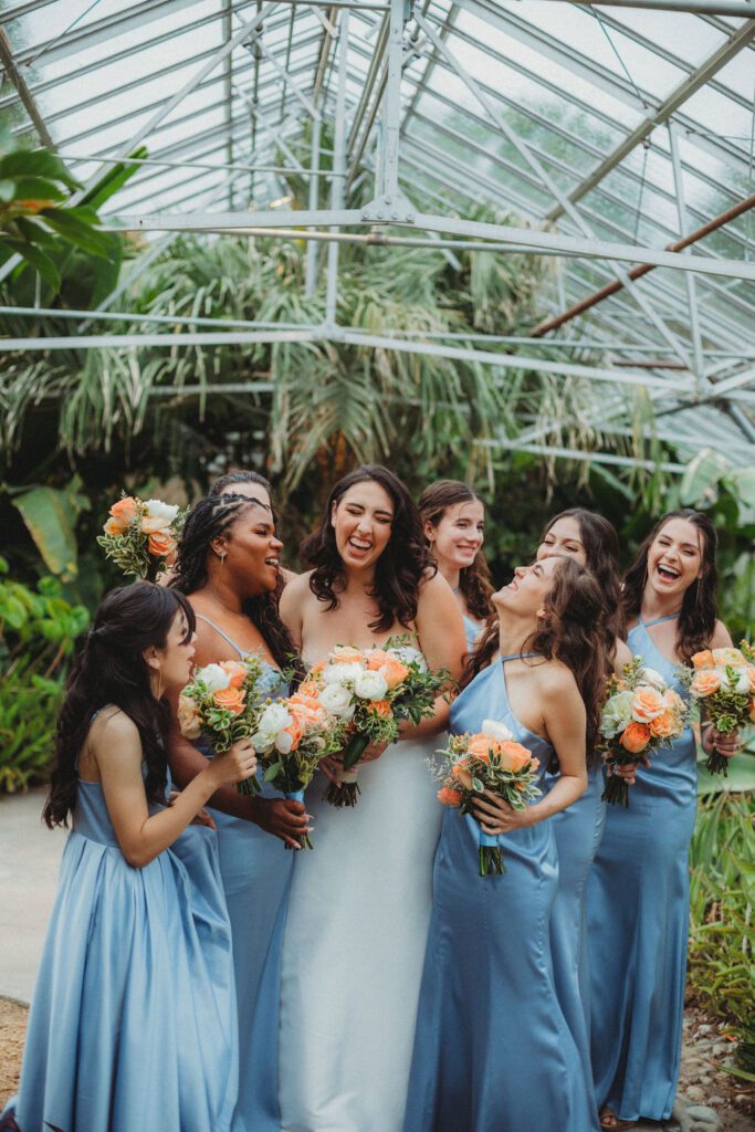 Bride and her bridesmaids hugging her in sweet greenhouse at Roger Williams Botanical Garden Park in Providence, Rhode Island.