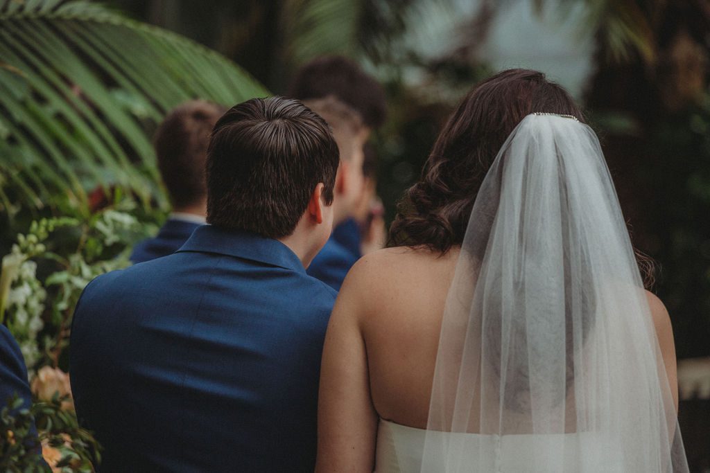 Bride and groom holding hands during romantic greenhouse in at Roger Williams Botanical Garden Park in Providence, Rhode Island.