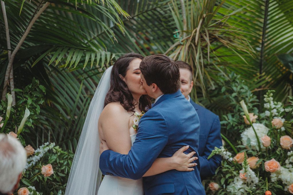 Bride and groom sharing their first kiss during romantic greenhouse wedding ceremony at Roger Williams Botanical Garden Park in Providence, Rhode Island.