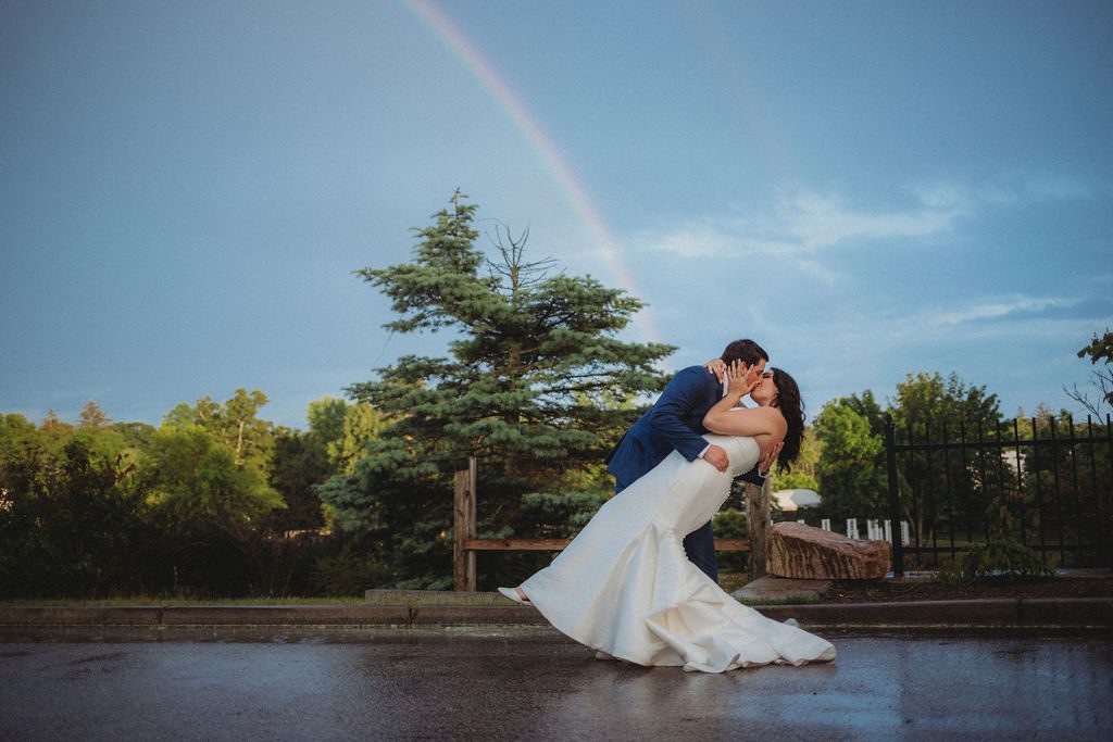 Bride and groom kissing under a rainbow at Roger Williams Botanical Garden Park in Providence, Rhode Island.