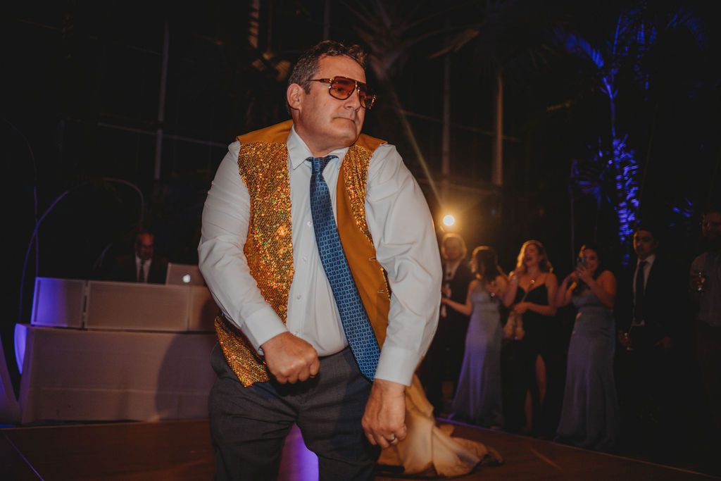 Father of the bride dancing with gold vest in greenhouse during reception at Roger Williams Botanical Garden Park in Providence, Rhode Island.
