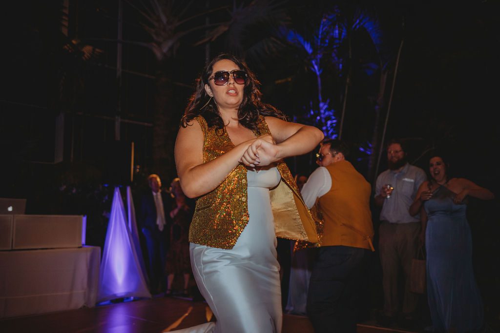 Bride dancing wearing a gold vest during wedding reception in greenhouse at Roger Williams Botanical Garden Park in Providence, Rhode Island.