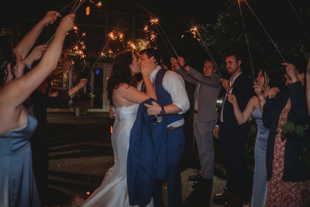 Bride and groom kissing with their guest holding sparklers at Roger Williams Botanical Garden Park in Providence, Rhode Island.