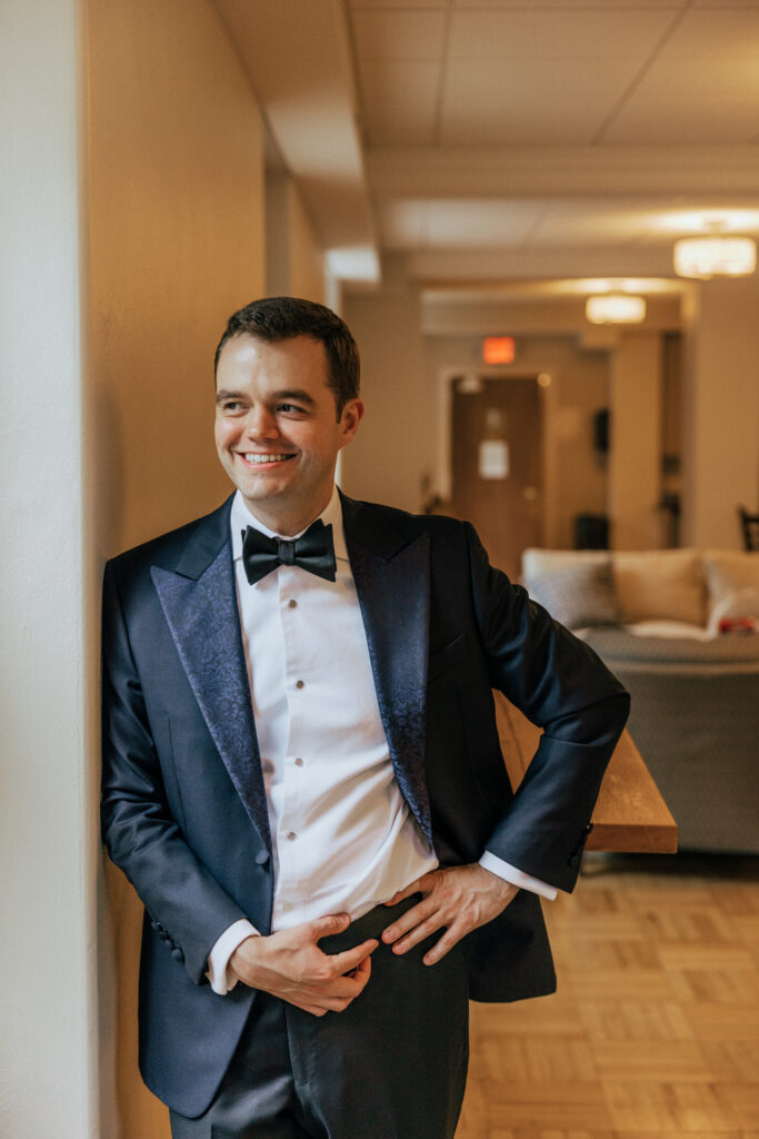 Groom leaning against wall and looking out the window smiling at The Conner Center in Dover, Massachusetts.