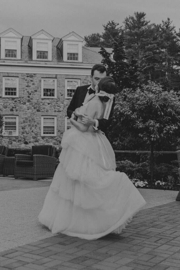 Bride and groom kissing in front of stone building at The Conner Center in Dover, Massachusetts.
