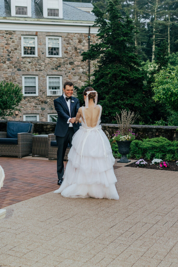 Bride and groom romantically holding hands and smiling at each other with stone castle behind them at The Conner Center in Dover, Massachusetts.
