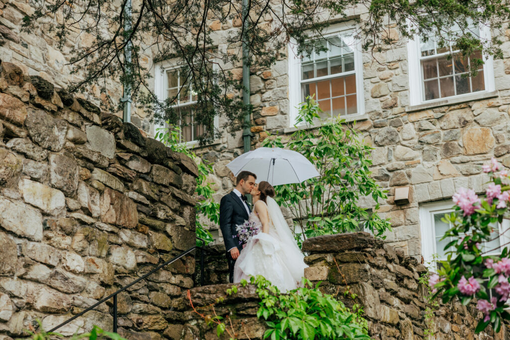 Romantic bride and groom kissing in stone castle under clear umbrella at The Conner Center in Dover, Massachusetts.