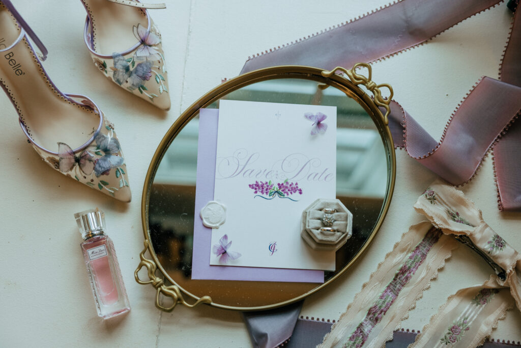 Whimsical flat lay of purple shoes, mirror, invitation, and rings at The Conner Center in Dover, Massachusetts.