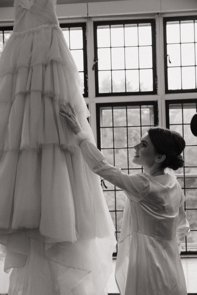 Bride touching her wedding dress in front of windows at The Conner Center in Dover, Massachusetts.