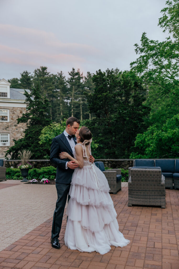 Bride and groom hugging and kissing during summer wedding with greenery and stone castle behind them at The Conner Center in Dover, Massachusetts.