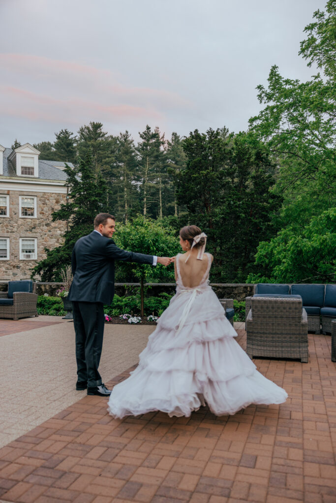 Groom spinning bride at summer wedding with greenery and stone castle behind them at The Conner Center in Dover, Massachusetts.