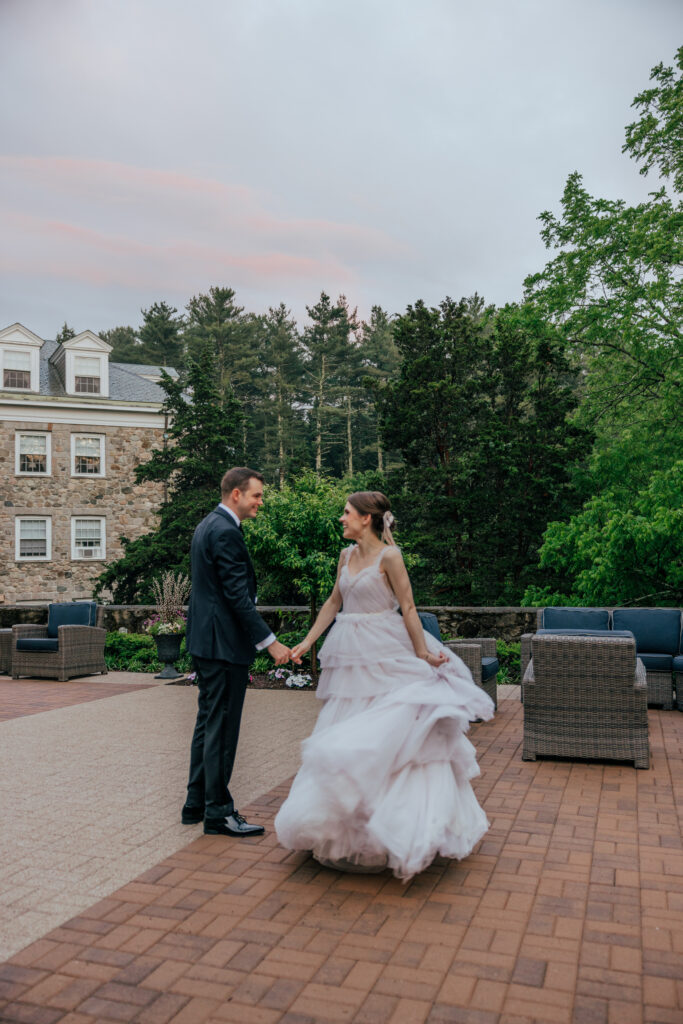 Groom spinning bride on balcony with stone building behind them at The Conner Center in Dover, Massachusetts.
