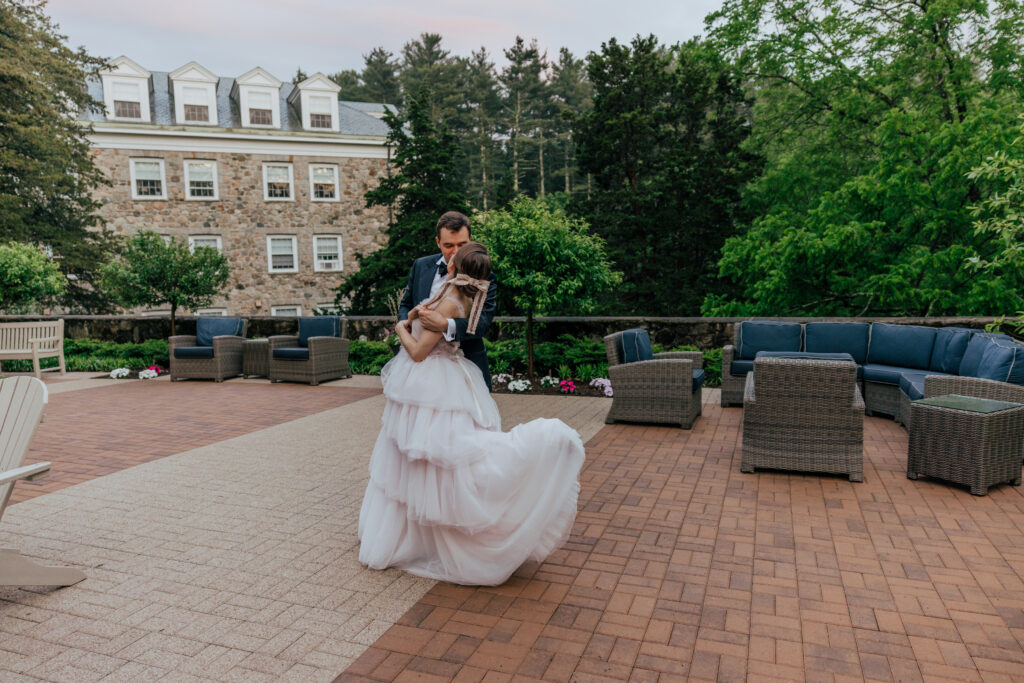 Groom spinning bride as she kicks her feet with greenery and castle in the background at The Conner Center in Dover, Massachusetts.