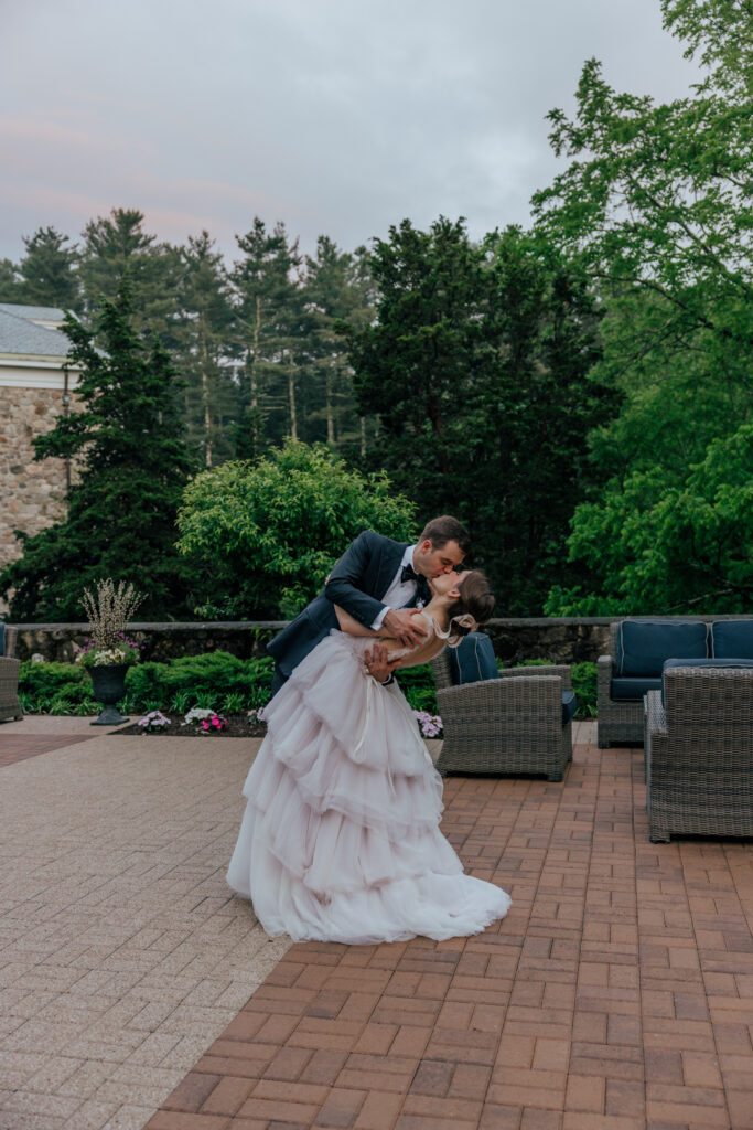 Groom dipping bride as they kiss with greenery and castle behind them at The Conner Center in Dover, Massachusetts.