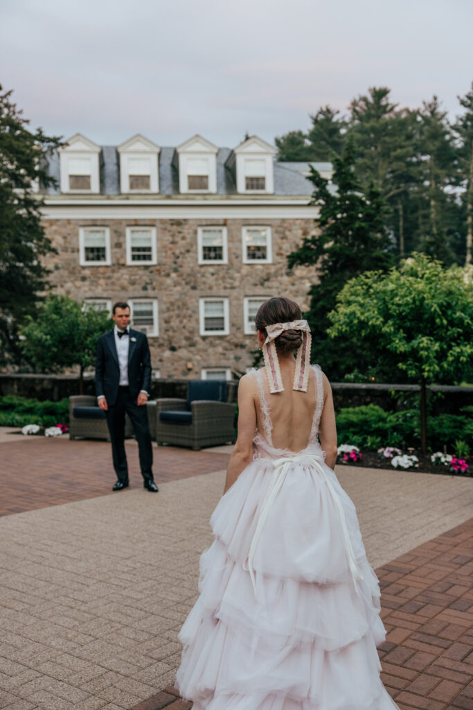 Bride looking walking towards groom as he smiles at her with stone castle behind them at The Conner Center in Dover, Massachusetts.